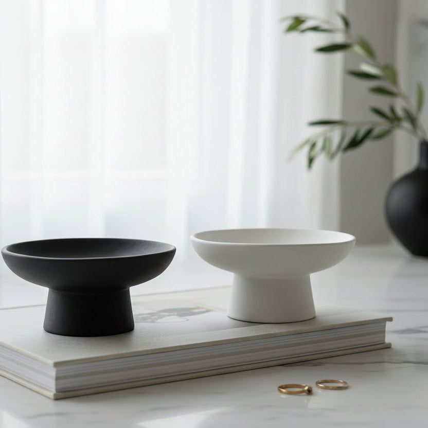 A black and a white highstem small trinket bowl sitting on a book in adecor