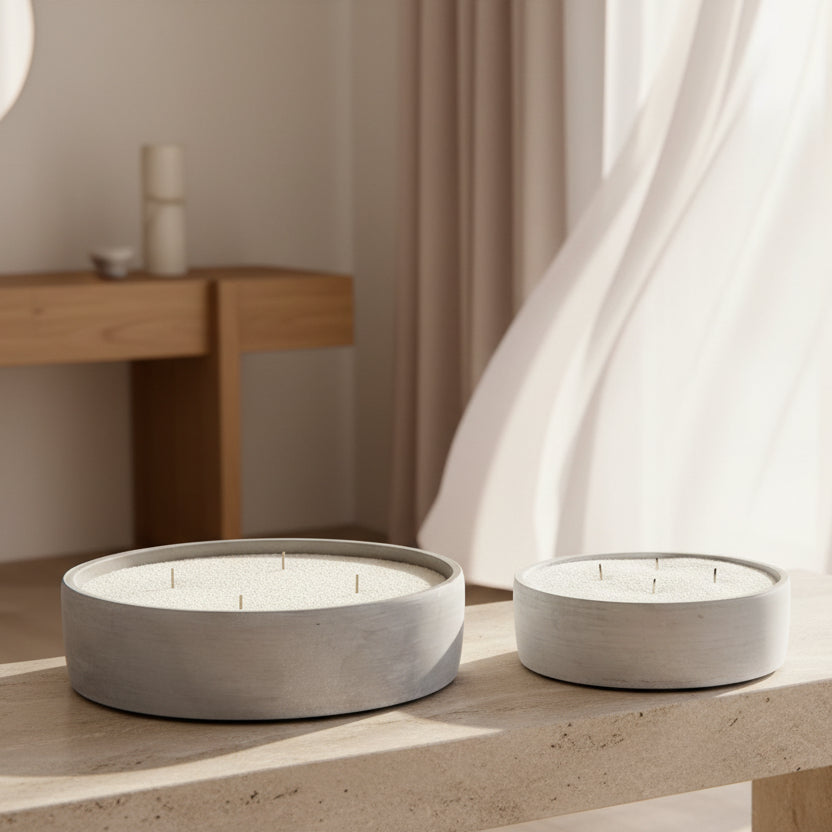 Two round white candle bowls in gray concrete colour, one larger and one smaller, placed on a stone bench