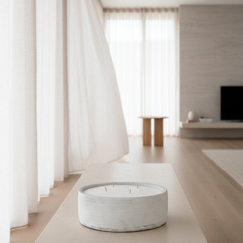 A round concrete textured CandleSand bowl with 4 wicks, filled with white sandwax, sits on a  table