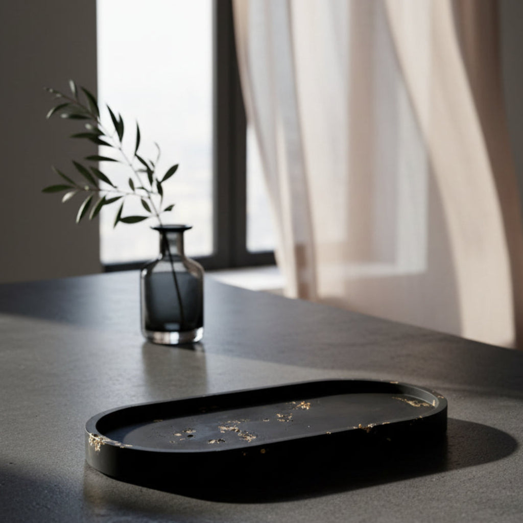 Black oval tray on a dark surface with a small vase and plant in the background.