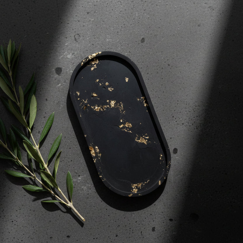 Black oval tray with gold speckles on a concrete surface