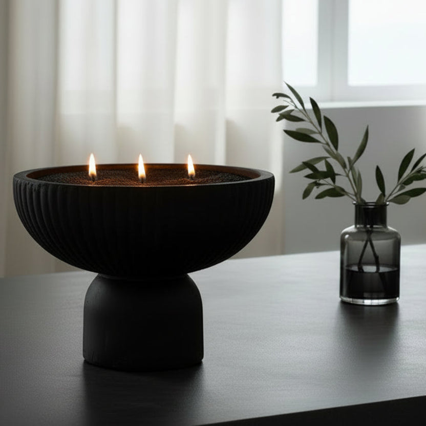 Ceramic bowl with black candlesand on a black surface in a moody room with white curtains.