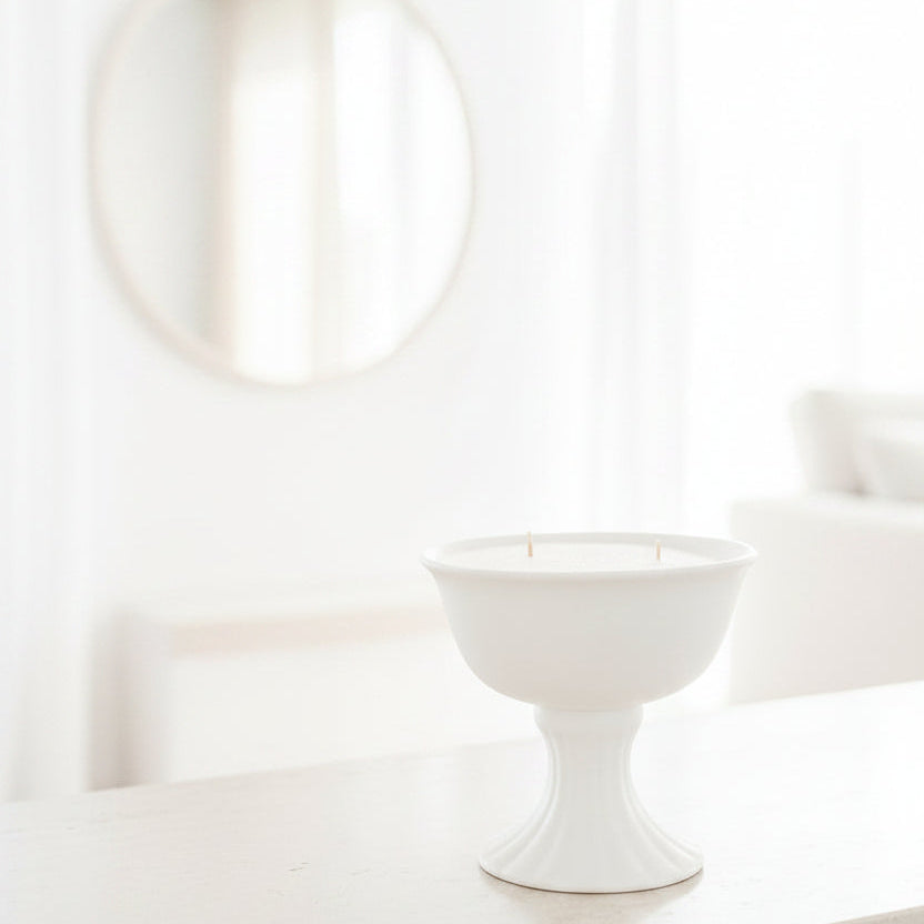A white ceramic pedestal candle holder with a fluted base, holding white sand candle